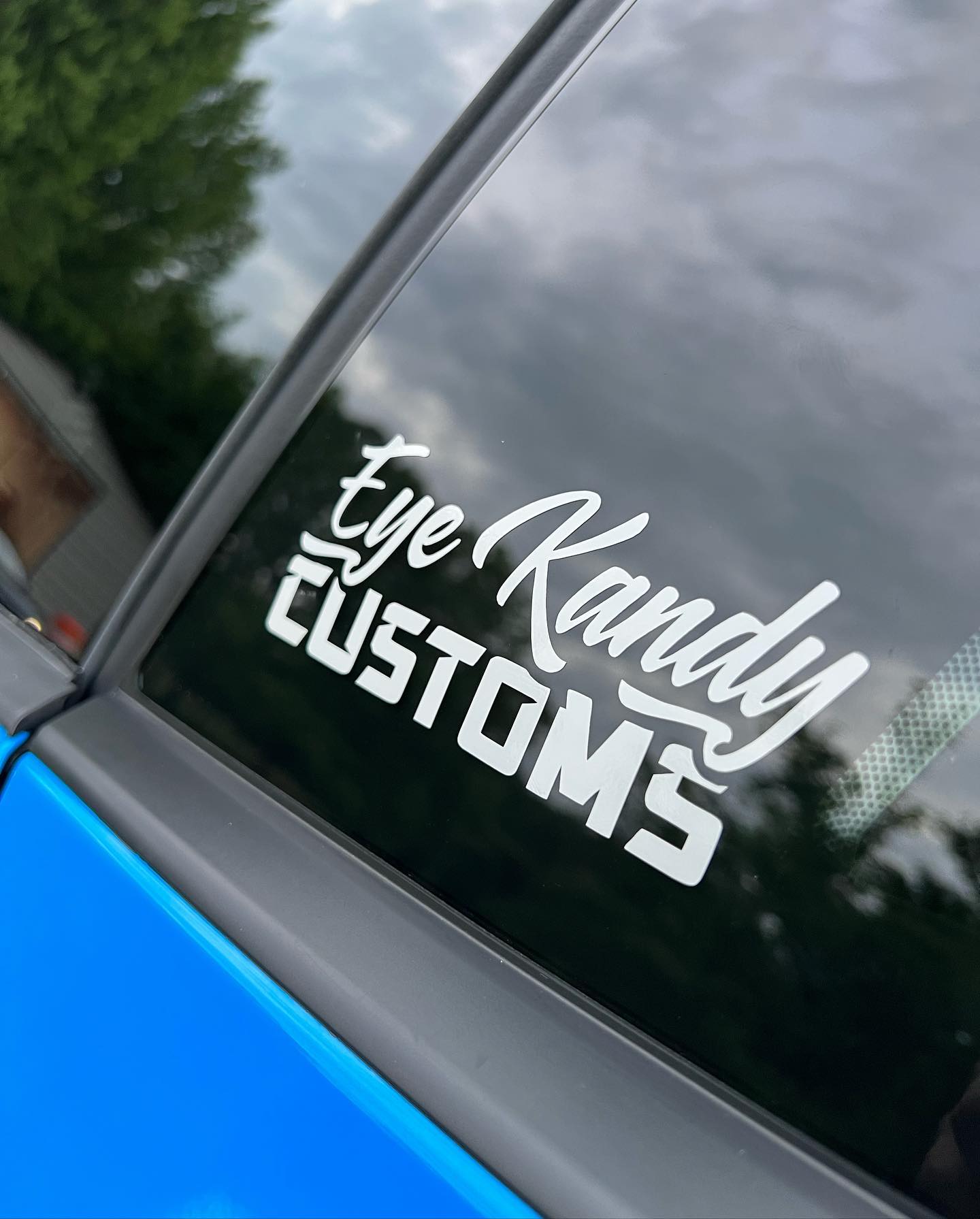 A white 'Eye Randy CUSTOMS' decal on a car window, featuring cursive and block lettering.
